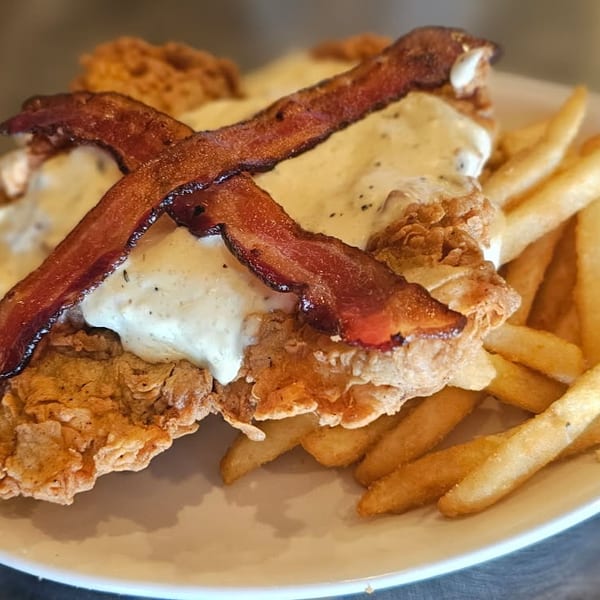 Crispy fried chicken topped with creamy sauce and bacon, served with golden French fries on a plate.