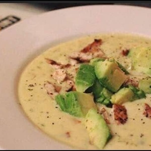 Creamy soup topped with diced avocado and chicken, with a Kenny's Burger Joint menu in the background.