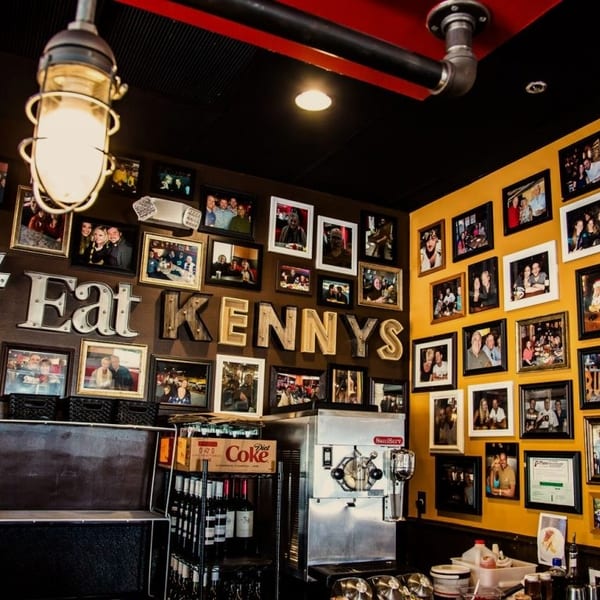 Restaurant interior with walls covered in framed photos and a large "#Eat Kennys" sign.