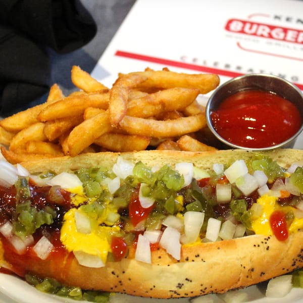 A hot dog with mustard, ketchup, relish, and onions, served with fries and ketchup.