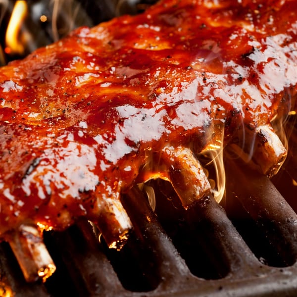 A rack of BBQ ribs, glistening with sauce, cooking on a fiery grill.