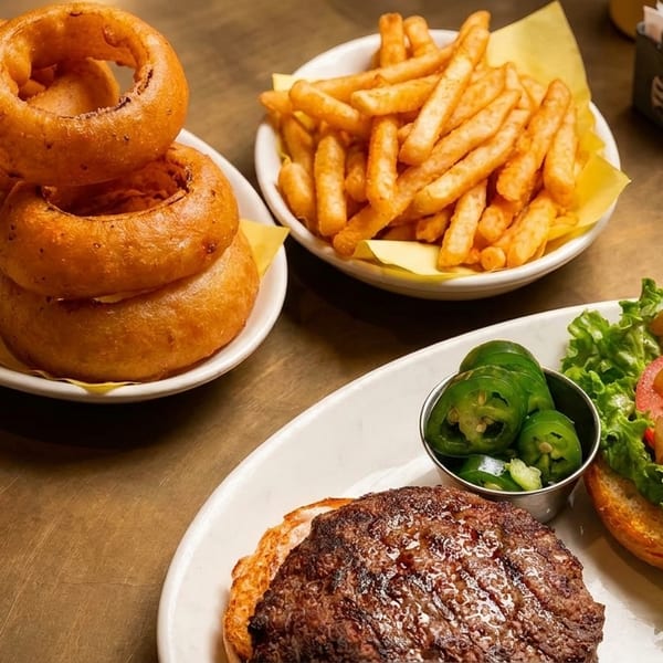 Cheeseburger, open-faced burger with caramelized onions, fries, onion rings, and jalapeños on a table.