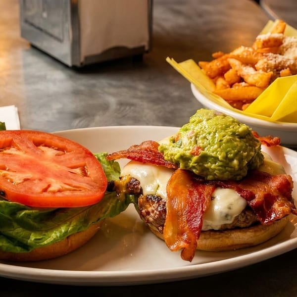 Gourmet burger with bacon, guacamole, and cheese, served with fries and a soda.