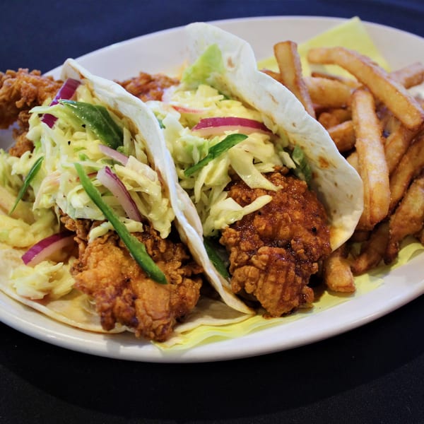 Two fried chicken tacos with slaw and red onion, served with a side of french fries.
