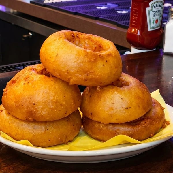 A plate of golden-brown onion rings on a bar counter with condiments and a drink.